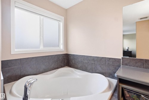 Corner soaking tub with deck-mounted chrome faucet, dark gray tiled surround, and frosted sliding window - 1444 37C Avenue, Edmonton, AB - Indoor Photo Showing Bathroom