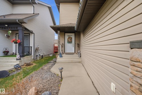 Exterior entry featuring a white paneled door, stone column accents, concrete walkway, and beige horizontal siding - 1444 37C Avenue, Edmonton, AB - Outdoor With Exterior