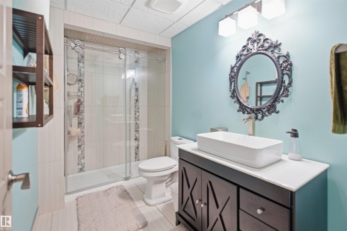 Bathroom featuring a dark wood vanity with a white countertop and vessel sink, a decorative framed mirror, and a glass-enclosed shower with tiled walls - 1444 37C Avenue, Edmonton, AB - Indoor Photo Showing Bathroom