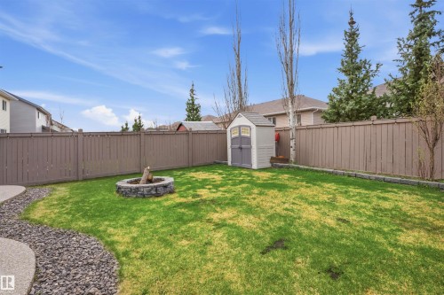 Expansive fenced backyard featuring a stone-lined fire pit, a garden shed, mature trees, and a curved concrete patio with decorative gravel - 1444 37C Avenue, Edmonton, AB - Outdoor