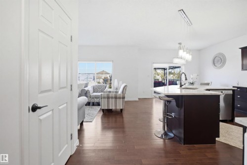 Open-concept interior featuring wood-finish flooring, a kitchen island with stone countertops, a modern linear pendant light fixture, and white paneled interior doors with dark hardware - 1453 Hays Way, Edmonton, AB - Indoor Photo Showing Kitchen