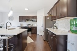 Kitchen featuring rich wood-finish cabinetry, light-toned countertops, and a white mosaic tile backsplash - 