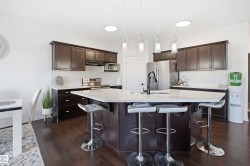 Kitchen featuring dark wood cabinetry, a white countertop island with seating, a mosaic tile backsplash, stainless steel appliances, and dark wood-finish flooring - 