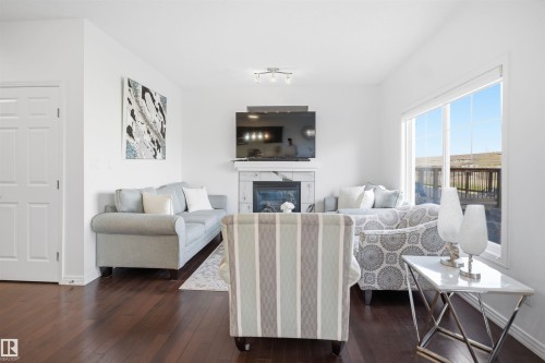 Living area featuring rich wood-finish flooring and a white marble-look fireplace with an electric insert - 1453 Hays Way, Edmonton, AB - Indoor Photo Showing Living Room With Fireplace