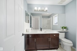 Bathroom featuring a dark wood-finish vanity with a white countertop and undermount sink, a large wall-mounted mirror, and a white toilet - 