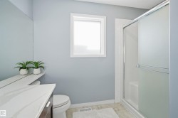 Bathroom featuring a frosted glass shower enclosure, white window frame, wood-finish vanity with a light-toned countertop, and light blue wall paint - 