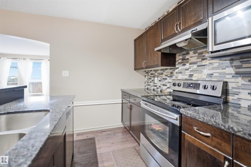 Kitchen featuring wood-finish cabinetry, stainless steel appliances, granite countertops, a mosaic tile backsplash, and wood-finish flooring - 1144 35 Avenue, Edmonton, AB - Indoor Photo Showing Kitchen With Stainless Steel Kitchen With Upgraded Kitchen