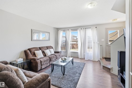 Living area featuring light gray walls, wood-finish flooring, and multiple windows with white curtains - 1144 35 Avenue, Edmonton, AB - Indoor Photo Showing Living Room