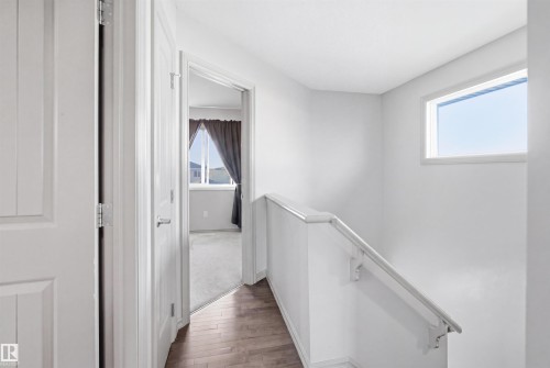 Bright upper-level hallway featuring wood-finish flooring, a white painted handrail, and a high horizontal window - 1144 35 Avenue, Edmonton, AB - Indoor
