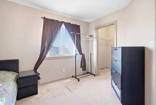Carpeted room with a window featuring dark curtains, light neutral walls, and a walk-in closet with wire shelving - 1144 35 Avenue, Edmonton, AB - Indoor