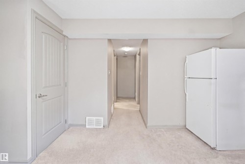 Neutral toned carpeting with light gray walls, a white paneled door with brushed nickel hardware, and a white refrigerator - 1144 35 Avenue, Edmonton, AB - Indoor Photo Showing Other Room