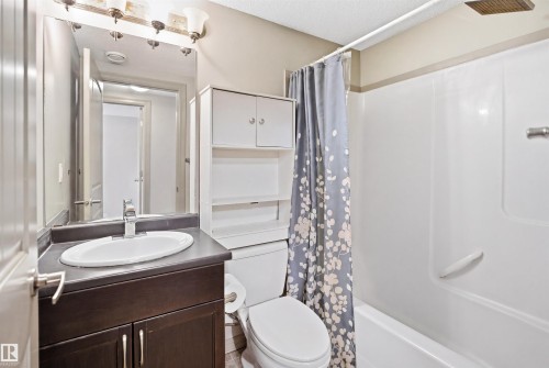 Full bathroom featuring a dark wood-finish vanity with a white oval undermount sink, a large mirror, a chrome faucet, and a combination tub and shower with a white surround - 1144 35 Avenue, Edmonton, AB - Indoor Photo Showing Bathroom