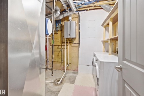 Dedicated utility space featuring a tankless water heater, exposed ductwork, washer, dryer, and built-in shelving - 1144 35 Avenue, Edmonton, AB - Indoor