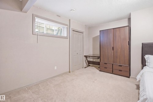 Carpeted room featuring a window with horizontal blinds, a closed bi-fold door, and a textured ceiling - 1144 35 Avenue, Edmonton, AB - Indoor