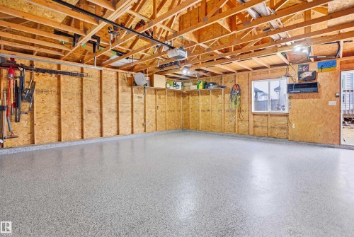 Spacious garage featuring a light speckled epoxy floor, exposed wood ceiling beams, and plywood walls - 1144 35 Avenue, Edmonton, AB - Indoor Photo Showing Basement