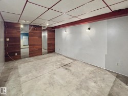 Spacious interior featuring a drop ceiling with recessed lighting, concrete flooring, wood-paneled accent wall, and wall-mounted sconces - 