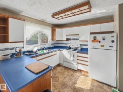 Kitchen featuring white cabinetry with wood trim, blue countertops, a double basin sink, white tile backsplash with decorative accents, and resilient flooring - 