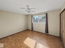 Spacious room featuring wood-finish flooring, a ceiling fan with integrated lighting, and a large window with privacy coverings - 