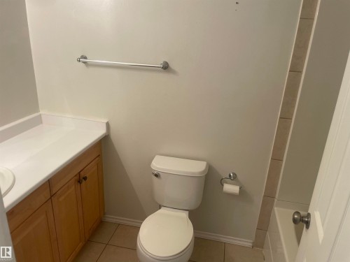 The bathroom features a vanity with a white countertop and wood cabinetry, a toilet, and tiled flooring - 2629 129A Avenue, Edmonton, AB - Indoor Photo Showing Bathroom