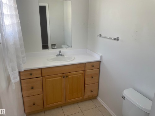 This bathroom features a light wood vanity with a white countertop and an integrated sink, complete with a mirror directly above - 2629 129A Avenue, Edmonton, AB - Indoor Photo Showing Bathroom