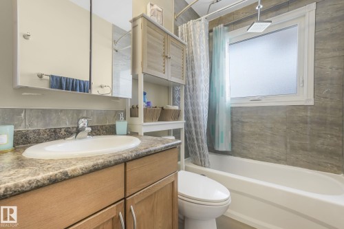 Bathroom featuring a built-in bathtub with tiled surround, a large window with privacy glass, wood-finish vanity with an integrated sink, laminate countertop, and medicine cabinet with mirrored doors - 2 Scarboro Place, St. Albert, AB - Indoor Photo Showing Bathroom
