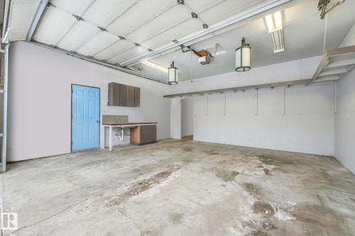 Spacious garage with a light blue access door, built-in cabinetry, a utility sink, and overhead storage shelving - 2 Scarboro Place, St. Albert, AB - Indoor Photo Showing Garage