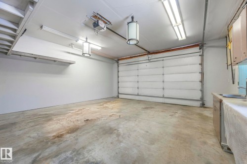 Spacious garage featuring a concrete floor, overhead fluorescent lighting, and two decorative pendant lights - 2 Scarboro Place, St. Albert, AB - Indoor Photo Showing Garage