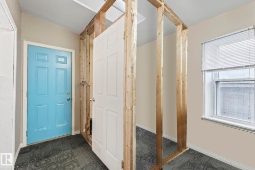 Interior space featuring a light blue panel door, exposed wood framing, a white paneled interior door, a window with blinds, and patterned carpet flooring - 2 Scarboro Place, St. Albert, AB - Indoor Photo Showing Other Room