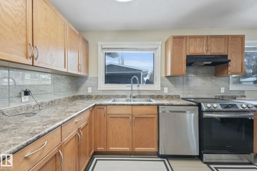 Kitchen featuring wood cabinetry, a stainless steel dishwasher, a black electric range, a double basin sink with a gooseneck faucet, and a tiled backsplash - 2 Scarboro Place, St. Albert, AB - Indoor Photo Showing Kitchen With Double Sink