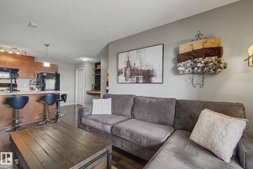 Open-concept living area featuring wood-finish flooring, a kitchen island with seating, integrated appliances, recessed lighting, and built-in shelving - 334 504 Albany Way, Edmonton, AB - Indoor Photo Showing Living Room