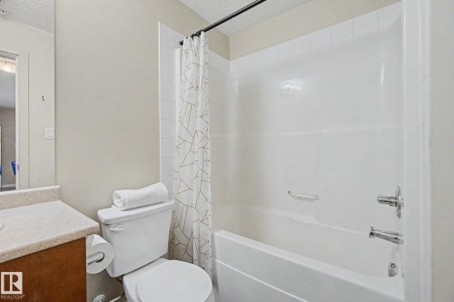 Bathroom featuring a white tub/shower combination with chrome fixtures, a light-toned vanity countertop, and a wood-finish vanity cabinet - 334 504 Albany Way, Edmonton, AB - Indoor Photo Showing Bathroom
