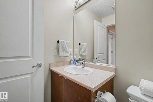 Bathroom featuring a wood-finish vanity with a light-toned countertop, an undermount sink with a chrome faucet, and a large wall-mounted mirror - 334 504 Albany Way, Edmonton, AB - Indoor Photo Showing Bathroom