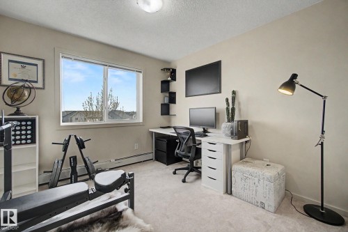 Carpeted room featuring a double-pane window, neutral-toned walls, built-in shelving, and baseboard heating - 334 504 Albany Way, Edmonton, AB - Indoor Photo Showing Office