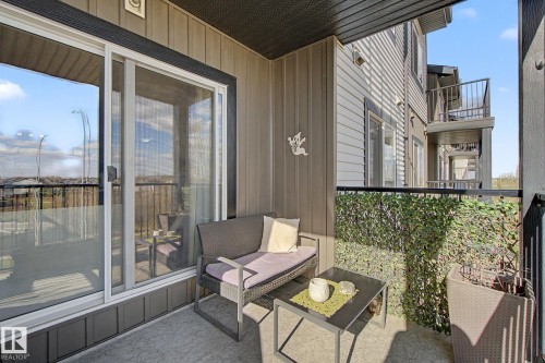 Balcony featuring a glass sliding door, textured exterior siding, black metal railings, and privacy screening - 334 504 Albany Way, Edmonton, AB - Outdoor With Balcony With Exterior