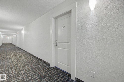 Hallway featuring a paneled entry door, textured walls, wall-mounted sconces, and patterned carpet flooring - 334 504 Albany Way, Edmonton, AB - Indoor Photo Showing Other Room