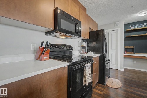 Kitchen featuring wood-finish cabinetry, white countertops, and black appliances - 334 504 Albany Way, Edmonton, AB - Indoor Photo Showing Kitchen