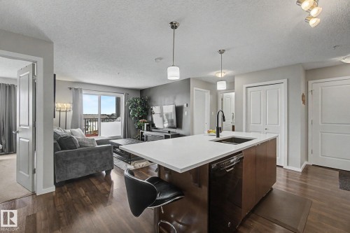 Open-concept living space featuring a kitchen island with a white countertop and dark wood-finish cabinetry, wood-finish flooring, and a sliding glass door to a balcony - 334 504 Albany Way, Edmonton, AB - Indoor Photo Showing Kitchen With Upgraded Kitchen