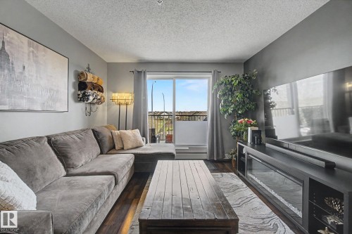 Spacious living area featuring wood-finish flooring, a built-in media console with a linear electric fireplace, and a sliding glass door opening to a private balcony - 334 504 Albany Way, Edmonton, AB - Indoor Photo Showing Living Room