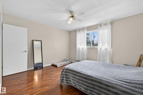 Room featuring wood-finish flooring, a ceiling fan with integrated lighting, and a window with white sheer curtains - 26E Meadowlark Village, Edmonton, AB - Indoor Photo Showing Bedroom