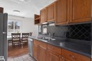 Kitchen featuring warm wood cabinetry, dark countertops, a black diamond-patterned tile backsplash, and a stainless steel double sink - 26E Meadowlark Village, Edmonton, AB  - Indoor Photo Showing Kitchen With Double Sink 