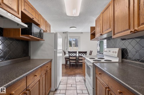 Kitchen featuring wood cabinetry, dark countertops, and a black tile backsplash - 26E Meadowlark Village, Edmonton, AB - Indoor Photo Showing Kitchen