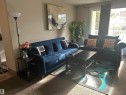 Living area featuring light beige wall paint, textured carpeting, and a large window with white framing - 204 10811 115 Street, Edmonton, AB  - Indoor Photo Showing Living Room 