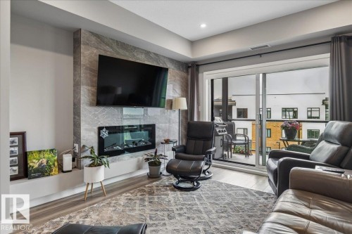 LINEAR ELECTRIC FIREPLACE WITH TILE SURROUND, SLIDING DOOR LEADING TO THE PATIO WITH SOLARIS POWERED SCREEN AND SPECTACULAR RAVINE AND DOWNTOWN VIEWS - 405 7463 May Common, Edmonton, AB - Indoor Photo Showing Living Room With Fireplace