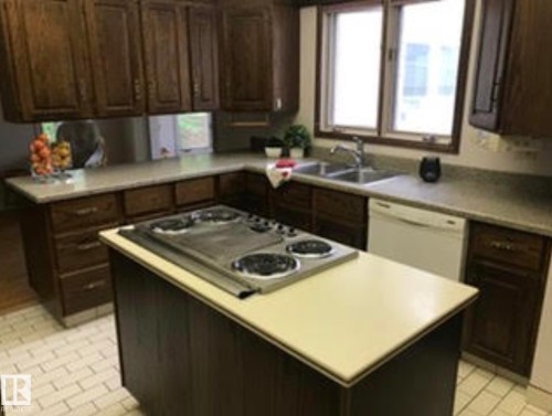 Kitchen featuring dark wood cabinetry, a central island with a built-in electric stovetop, double basin sink, and a white dishwasher - 9126 117 Street, Edmonton, AB 