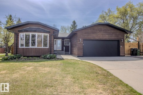 Wood-sided property featuring a concrete driveway and an attached single-bay garage with a black door - 3412 110 Street, Edmonton, AB - Outdoor