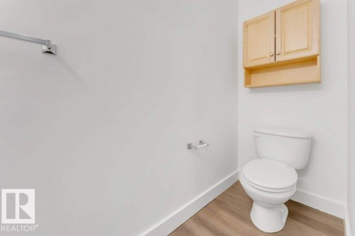 Powder room featuring a white toilet, light wood-finish flooring, and a natural wood-finish wall cabinet with storage - 7403 Singer Landing Landing, Edmonton, AB - Indoor Photo Showing Bathroom