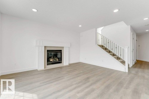 Spacious room featuring wood-finish flooring, a white mantel fireplace, recessed lighting, and a staircase with white balusters and dark metal spindles - 7403 Singer Landing Landing, Edmonton, AB - Indoor Photo Showing Living Room With Fireplace