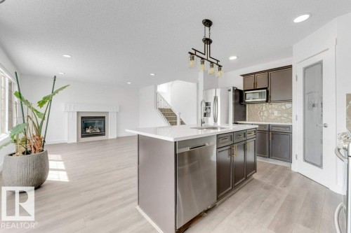 Kitchen island with integrated stainless steel sink and dishwasher, complemented by a contemporary chandelier - 7403 Singer Landing Landing, Edmonton, AB - Indoor Photo Showing Kitchen With Upgraded Kitchen