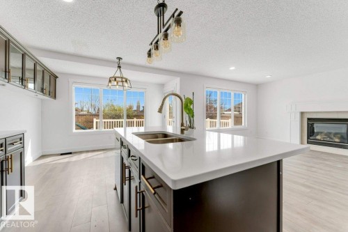 Kitchen island featuring a quartz countertop, double basin sink with a gooseneck faucet, and dark cabinetry - 7403 Singer Landing Landing, Edmonton, AB - Indoor With Fireplace
