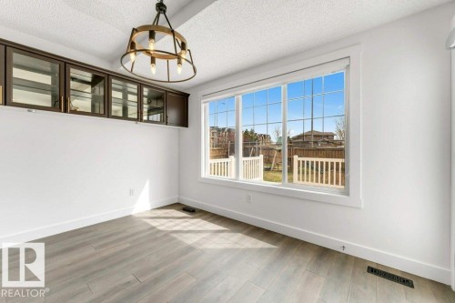 Spacious room featuring wood-finish flooring, white trim, and a large window with multiple panes - 7403 Singer Landing Landing, Edmonton, AB - Indoor Photo Showing Other Room